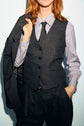 Person wearing a pinstripe gilet de tailleur, dress shirt, tie, and matching flanelle grise pants holds a suit jacket over their shoulder. Their other hand is in their pocket, completing a look classique chic. Face is partially visible.