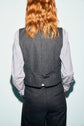 A person with wavy reddish hair, seen from behind, embodies a look classique chic by wearing a flanelle grise gilet de tailleur and matching trousers over a light-colored, long-sleeve shirt.