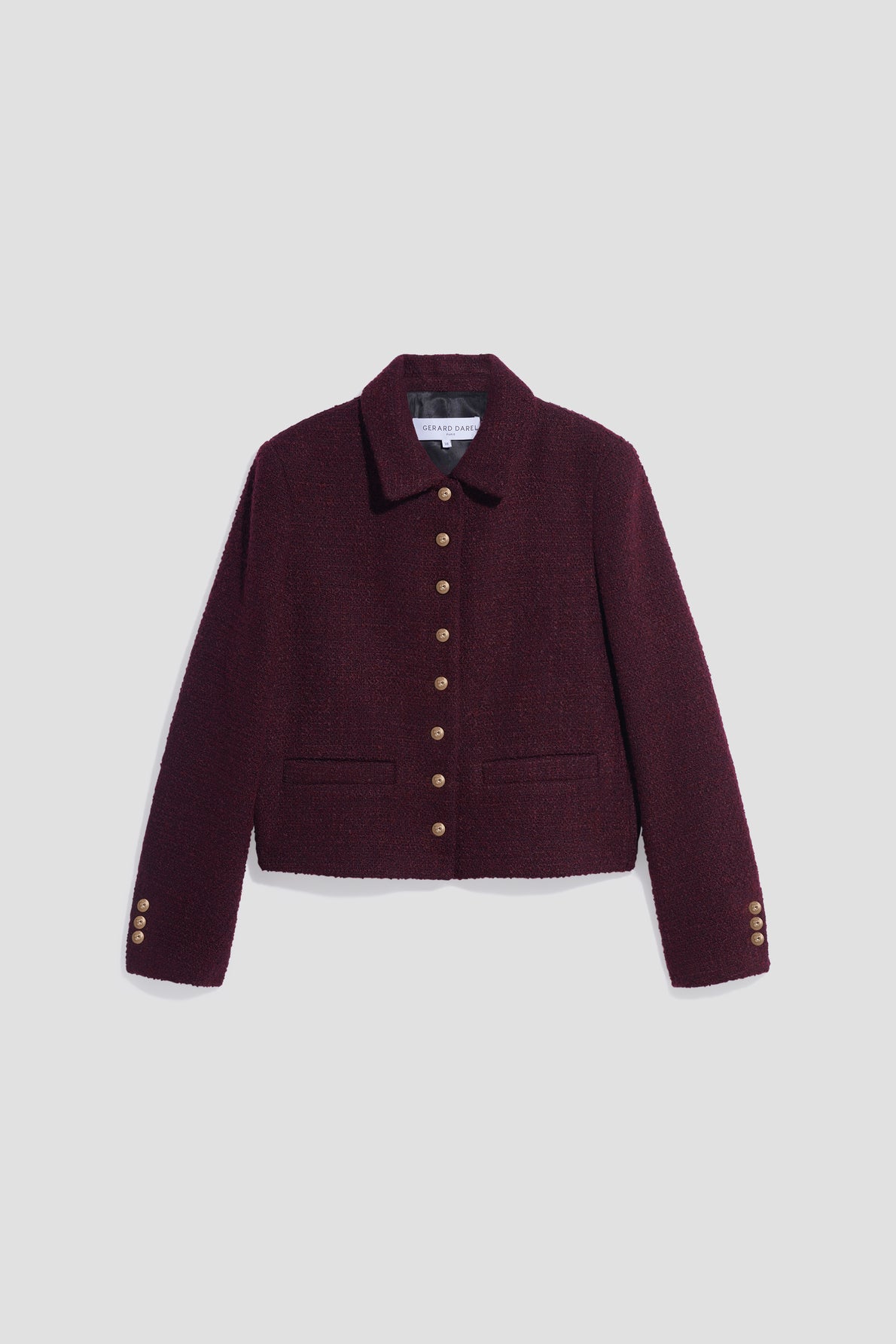 A cropped, dark burgundy veste tweed bouclé with gold buttons down the front and on the sleeves, featuring a collar and two front pockets, displayed on a plain light gray background.