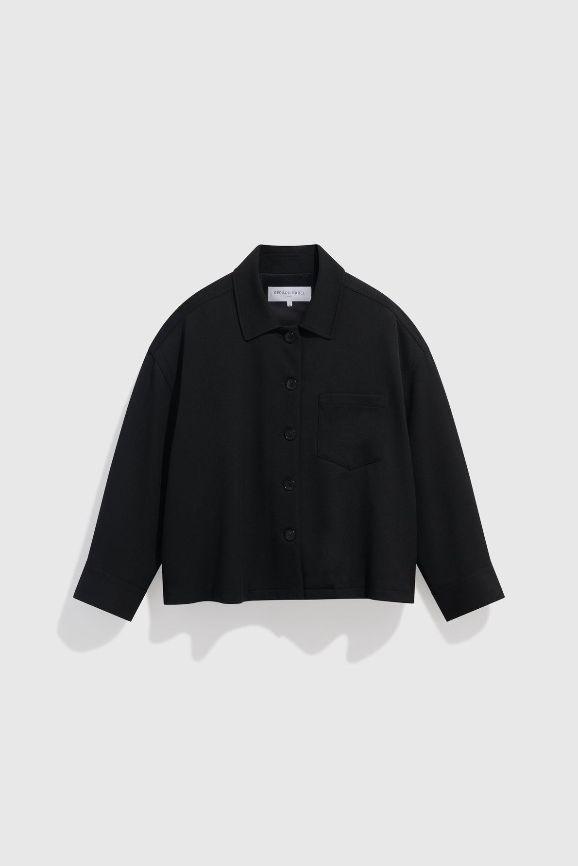A black, long-sleeve, button-up surchemise noire with a collar and a single chest pocket, displayed against a plain white background—a perfect blend of workwear utility and chemise chic style.