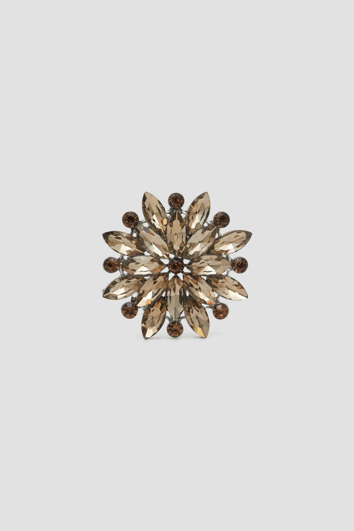 A gold and smoky brown jeweled broche élégante in a floral, starburst pattern with marquise and round crystal stones, set against a plain light gray background.