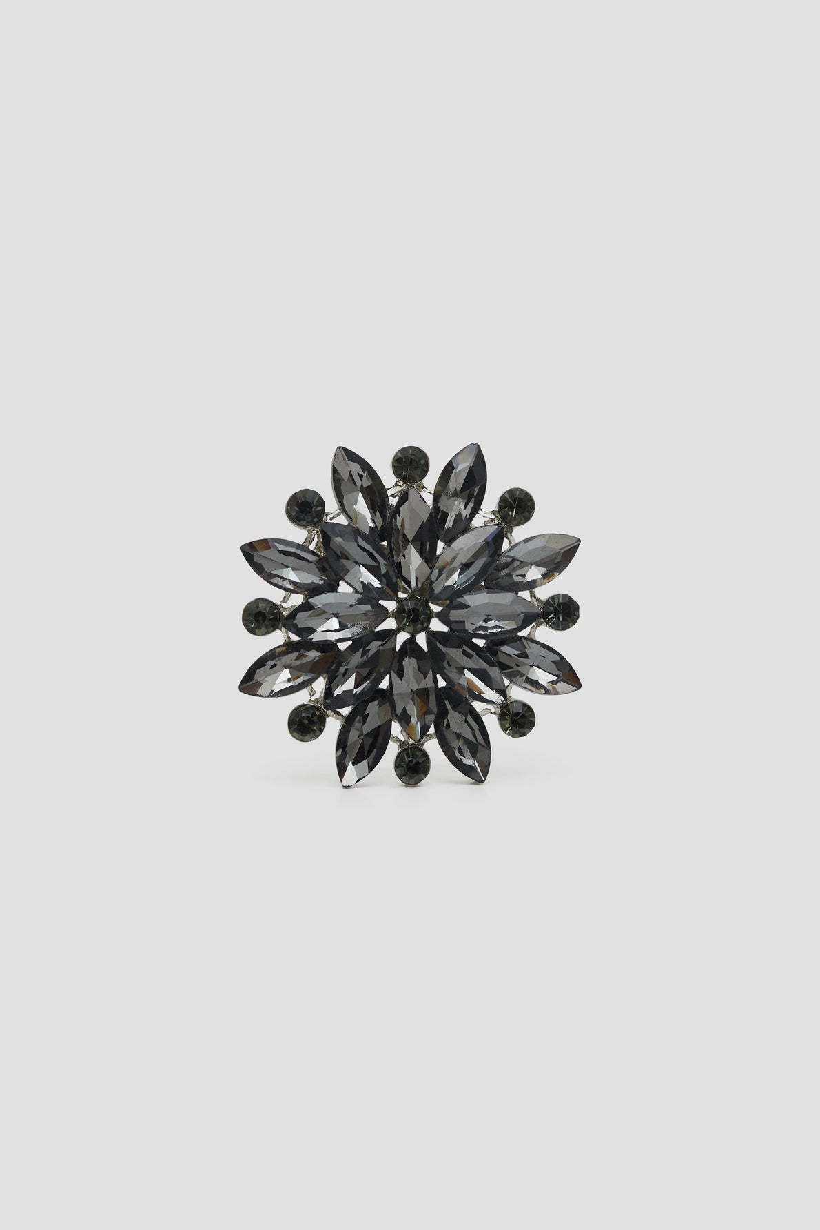 A round, flower-shaped broche corolle featuring dark, marquise-cut crystals arranged in layers, radiating from the center with small round crystals on the outer edge, set against a plain light gray background. This broche élégante adds a refined touch to any ensemble and is perfect as a broche veste for sophisticated styling.