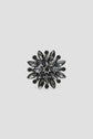 A round, flower-shaped broche corolle featuring dark, marquise-cut crystals arranged in layers, radiating from the center with small round crystals on the outer edge, set against a plain light gray background. This broche élégante adds a refined touch to any ensemble and is perfect as a broche veste for sophisticated styling.