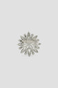 Silver-toned brooch with a floral, snowflake-like design, featuring petal-shaped and round decorative elements, shown against a plain light gray background. This broche élégante has a pin clasp visible on the back, making it an ideal accessory for adding refined charm to your veste.