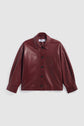 A maroon faux leather surchemise femme with a collar, front buttons, long sleeves, and a single chest pocket, displayed against a light gray background. This élégante veste bordeaux effortlessly combines style and versatility for any occasion.