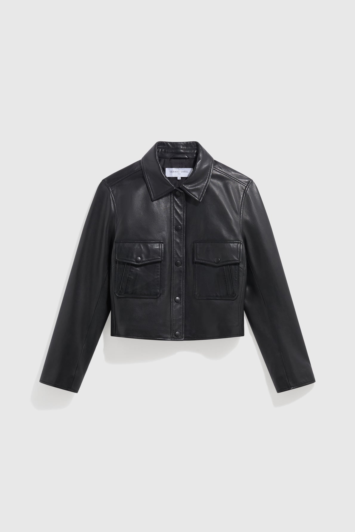 A black, cropped faux leather jacket with a collar, front snap buttons, and two chest flap pockets is displayed against a plain light gray background, capturing the essence of style vintage for a modern take on the classique veste cuir noir.