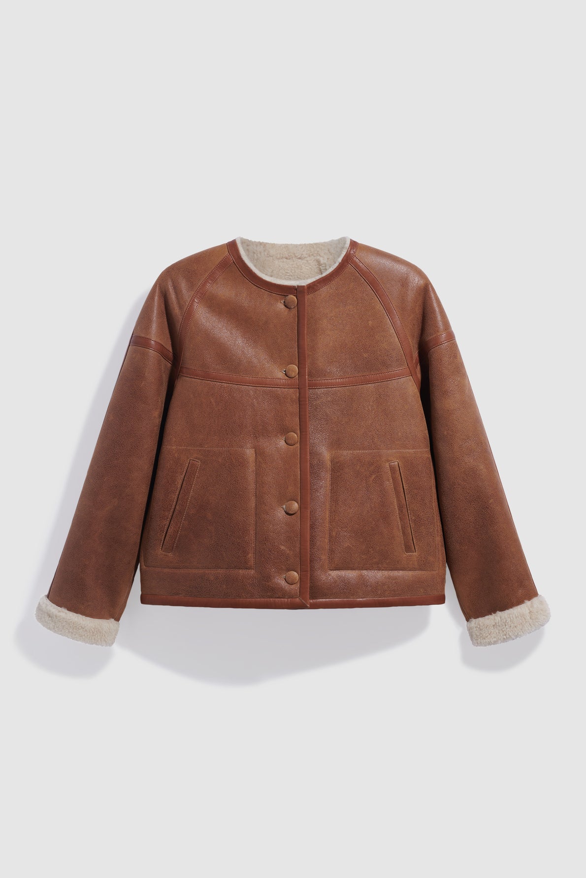Brown leather jacket with front buttons, two pockets, and cream shearling lining visible at the cuffs, this blouson cuir agneau is displayed against a plain light background.