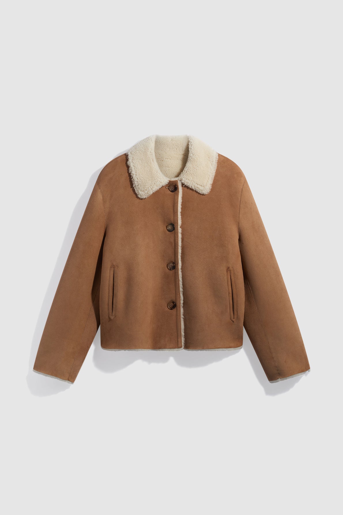 A tan suede jacket crafted from manteau cuir agneau with a plush white shearling collar, button front, and two side pockets, laid flat on a light gray background.