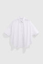 A loose-fitting white chemise oversize with short sleeves, a classic collar, and a curved hem crafted from popeline de coton, displayed on a plain light gray background.