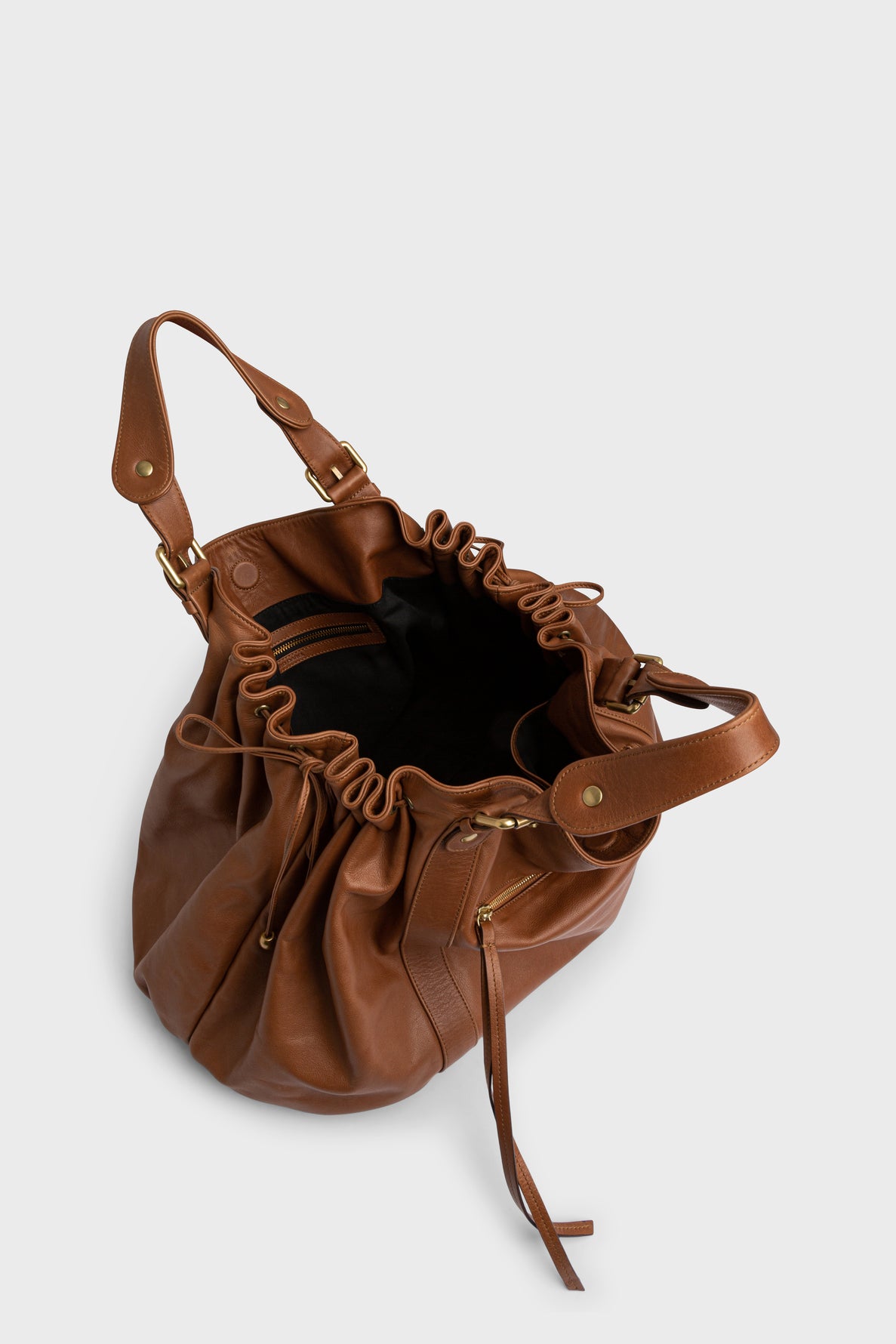 Brown leather sac à main with gold hardware, featuring a drawstring closure, crafted from cuir doux. The bag opens to reveal a black fabric interior and an inside zip pocket, photographed on a light gray background—perfect for carrying your essentials in style for 72h and beyond.