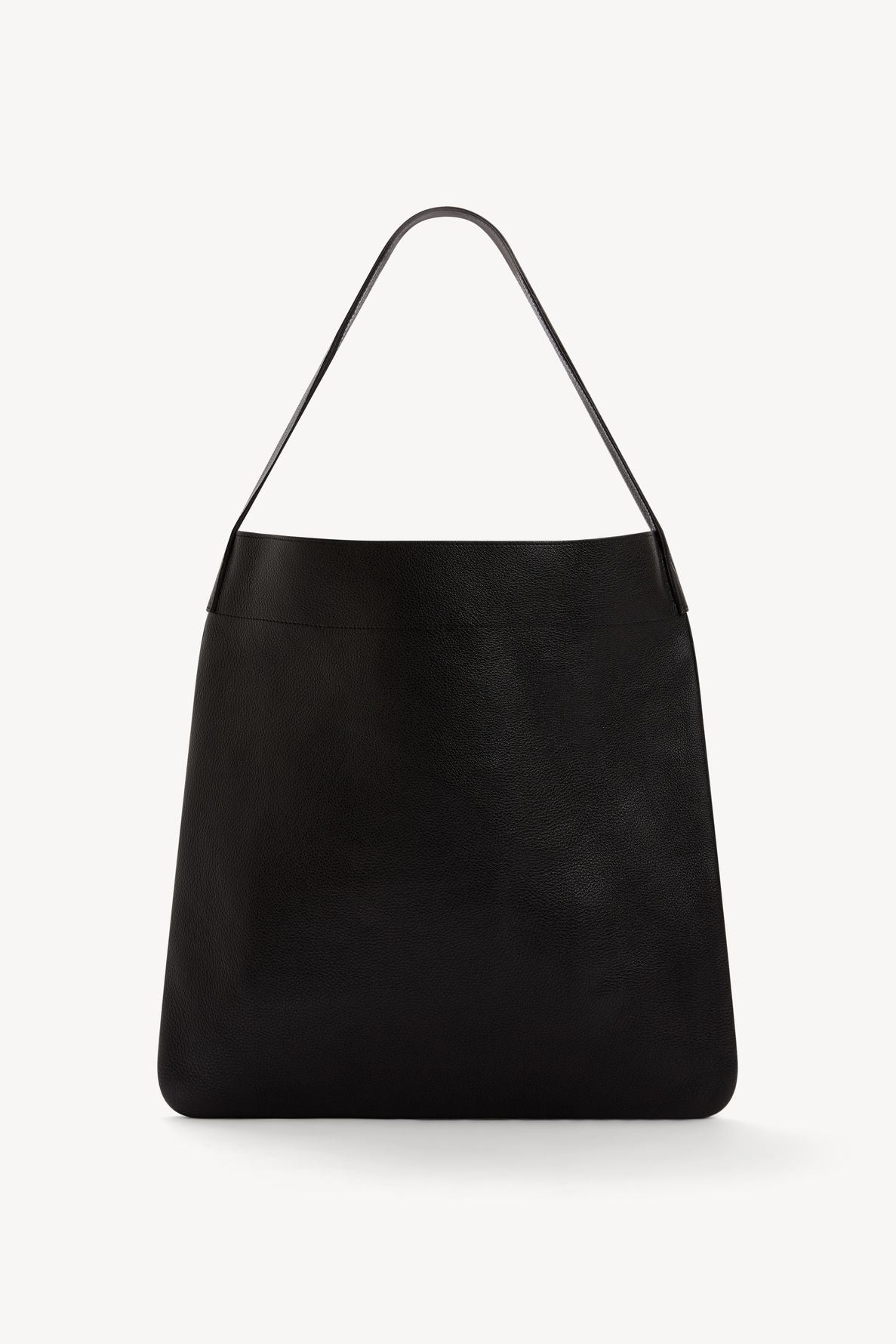 A large black cuir grainé leather tote bag with a single flat shoulder strap, minimalistic design, and a smooth, slightly textured surface, displayed against a plain white background.