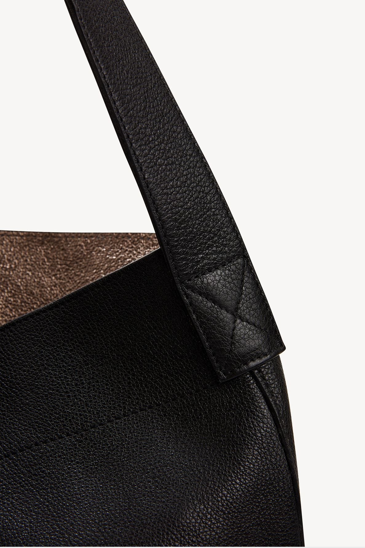 Close-up of a black cuir grainé leather bag with a textured surface, showing the strap attached to the body with detailed stitching. The bag’s interior lining is brown and slightly visible at the top edge, evoking the timeless allure of a sac hobo.