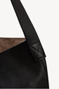 Close-up of a black cuir grainé leather bag with a textured surface, showing the strap attached to the body with detailed stitching. The bag’s interior lining is brown and slightly visible at the top edge, evoking the timeless allure of a sac hobo.