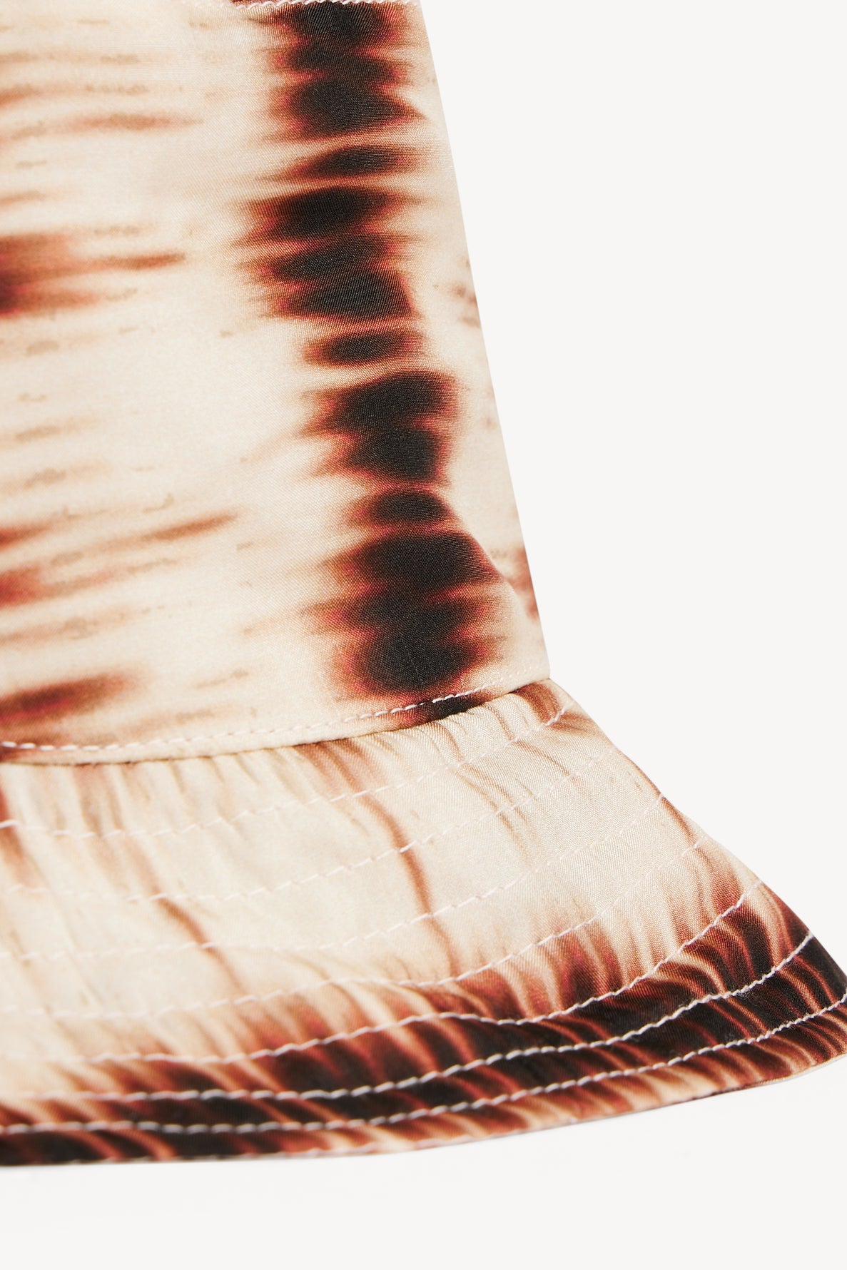 Close-up of a beige and brown tie-dye bucket hat, featuring an imprimé tie and dye pattern and detailed bord surpiqué that highlights the intricate stitching and fabric texture.