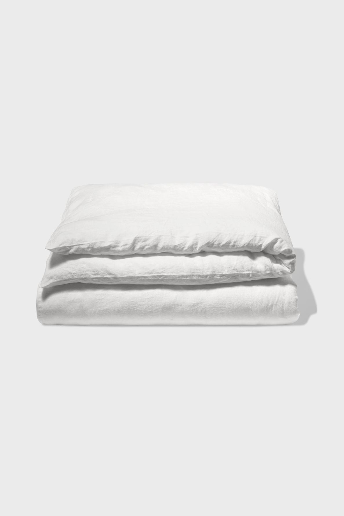 A neatly folded white duvet cover and matching pillowcase set, crafted from luxurious lin lavé blanc, displayed on a plain light gray background.