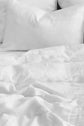 White pillows and a slightly wrinkled white bed sheet on a bed, accented by a housse de couette lin lavé blanc, create a clean and cozy appearance.