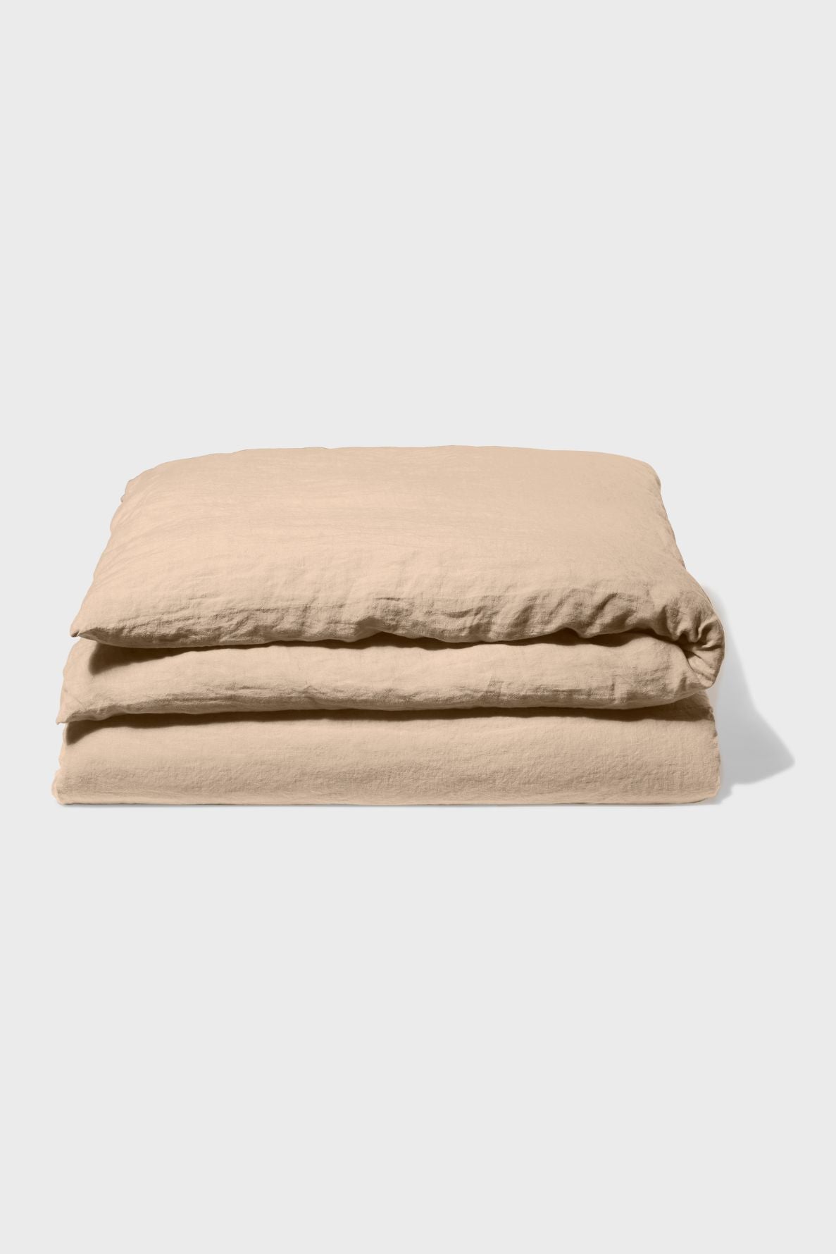 A folded beige linen duvet cover is placed on a plain light gray background, casting a soft shadow to the right.