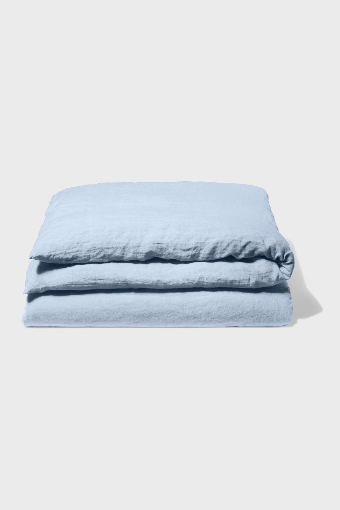 A folded light blue blanket or duvet lies on a plain, light-colored surface with a shadow cast to the right.