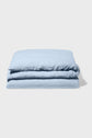 A folded light blue blanket or duvet lies on a plain, light-colored surface with a shadow cast to the right.
