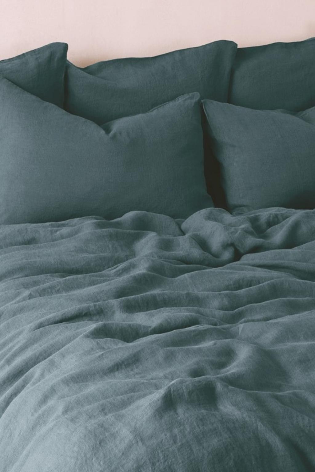 A neatly made bed with teal sheets and multiple matching pillows against a light-colored wall.