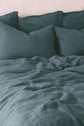 A neatly made bed with teal sheets and multiple matching pillows against a light-colored wall.