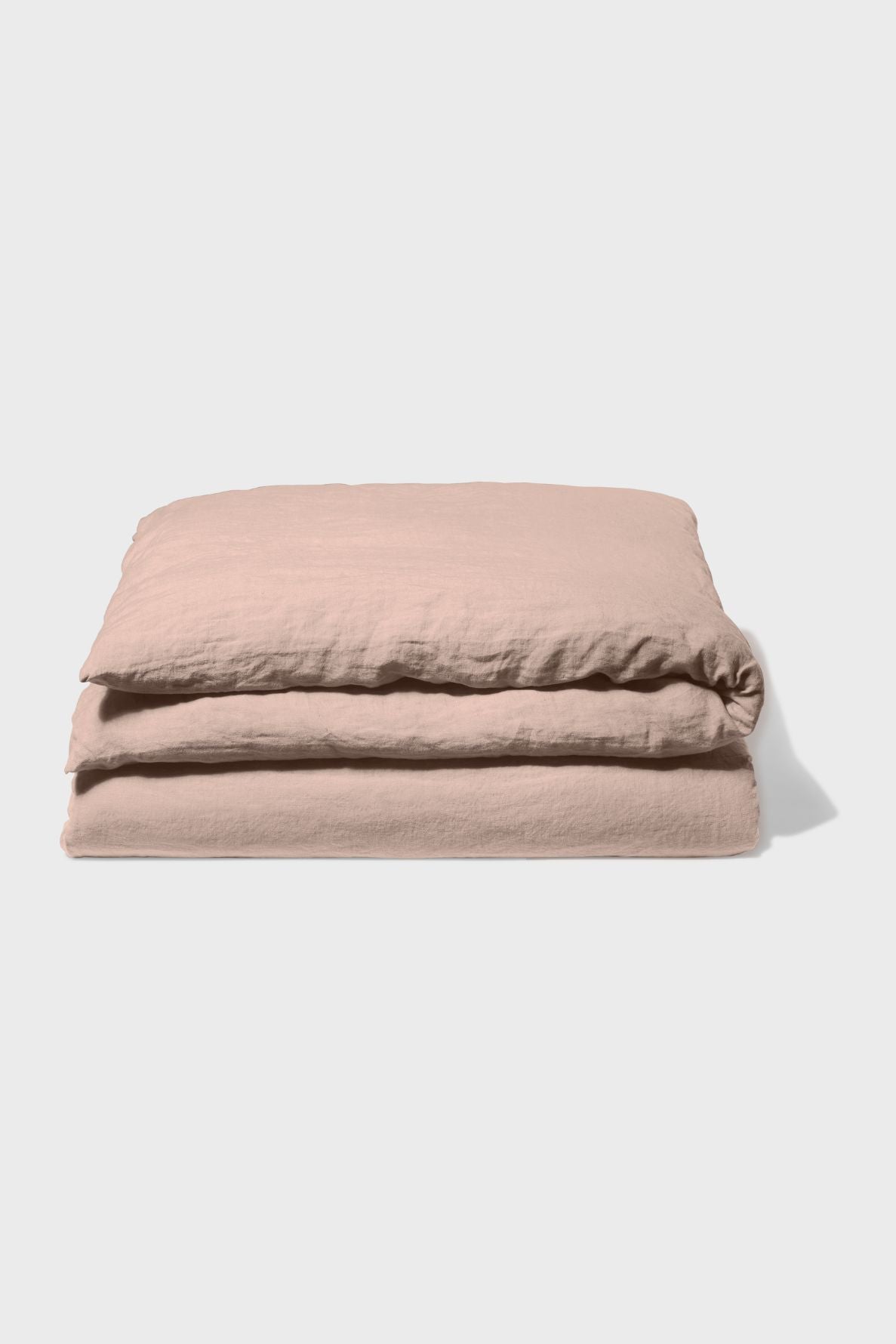 Folded light pink duvet cover made of soft, textured fabric, neatly stacked on a plain white background.