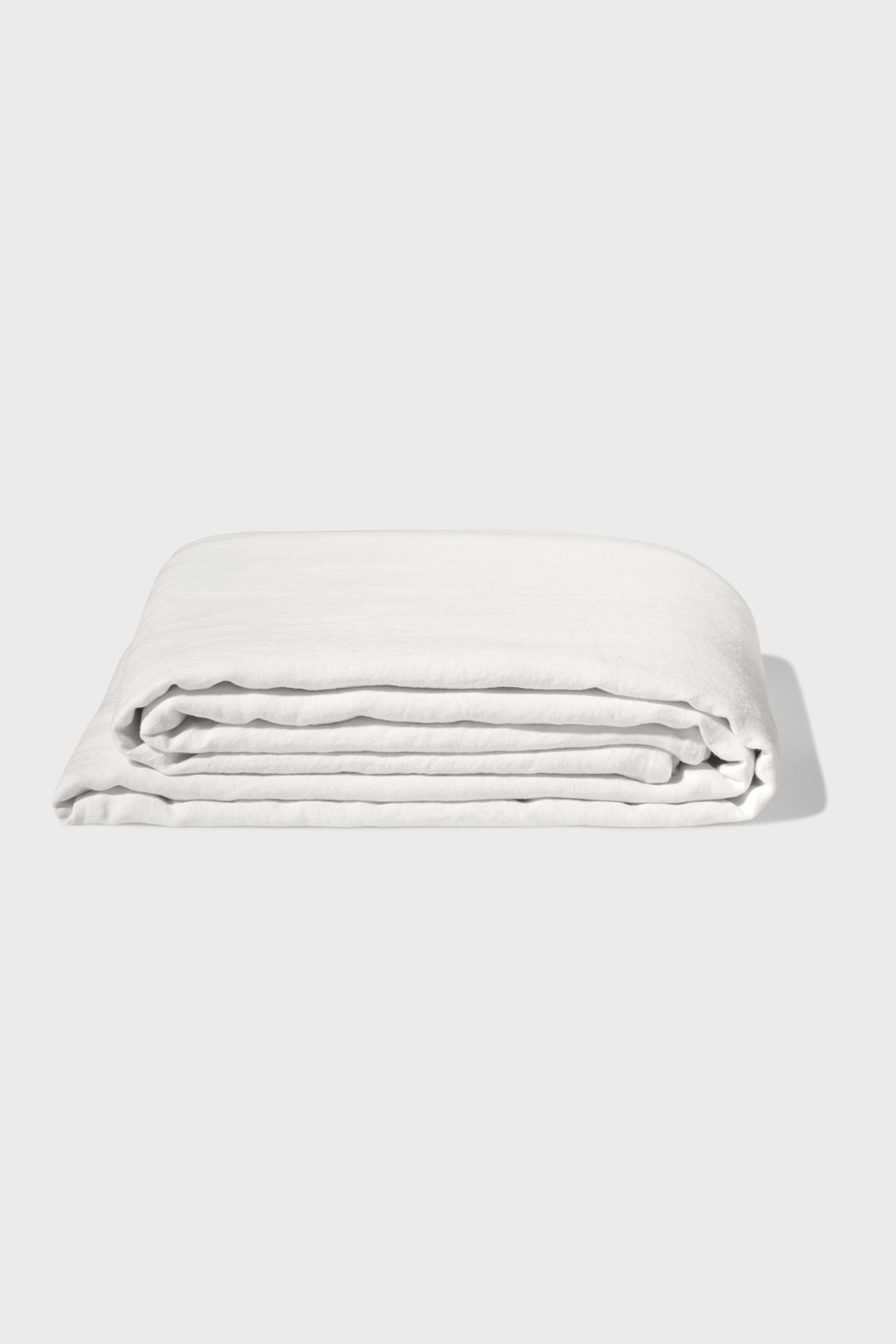 A neatly folded white bed sheet is displayed against a plain white background, with soft shadows visible to the right.
