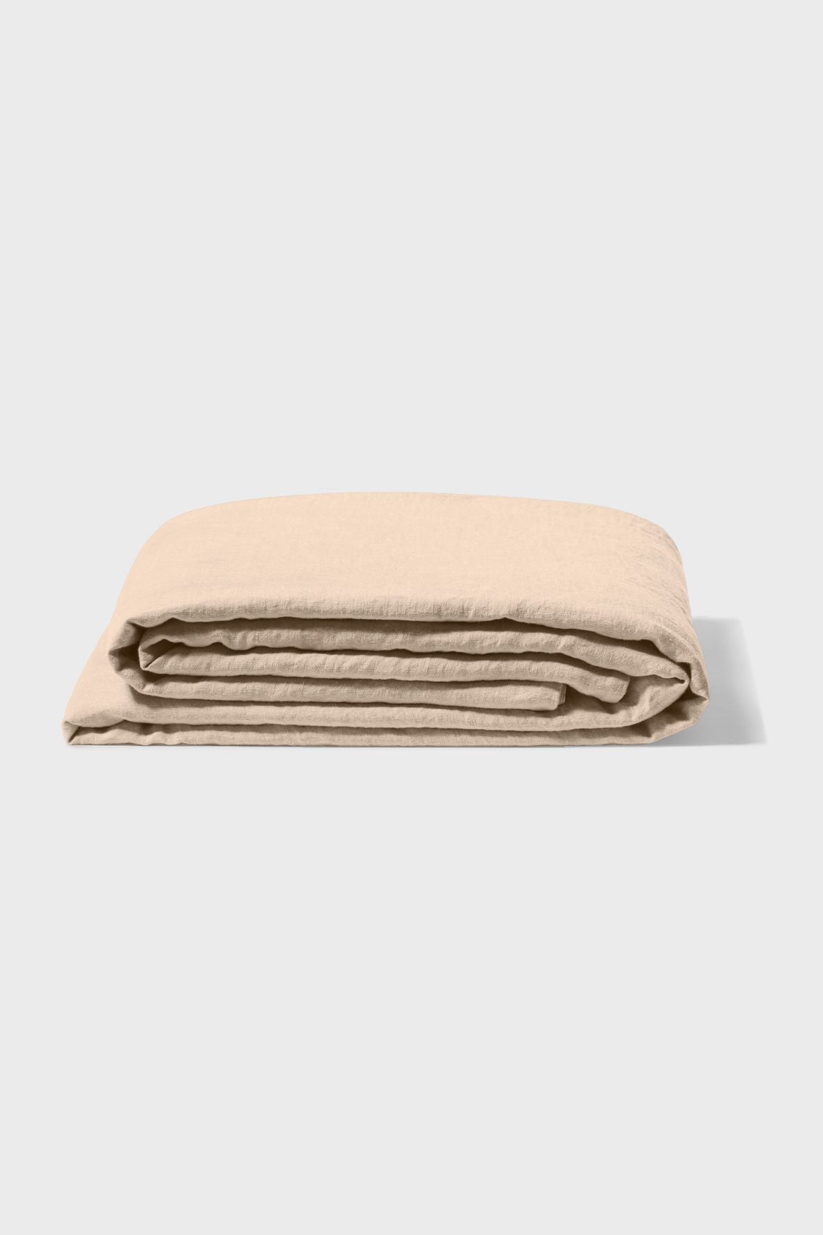 A neatly folded beige bedsheet is placed on a plain, light-colored surface, with soft shadows on the right side.