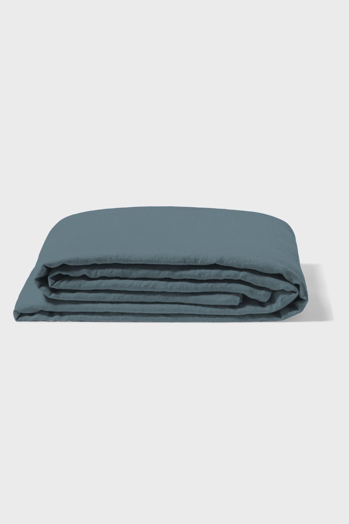 A neatly folded blue blanket lies on a flat, light-colored surface with a plain white background.