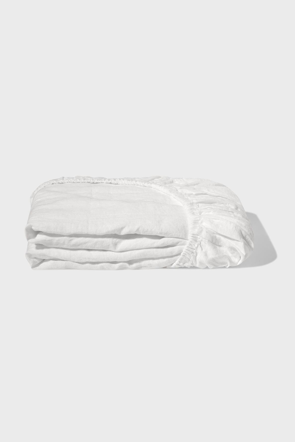 A neatly folded white fitted bed sheet with visible elastic edges, placed on a plain light grey background.