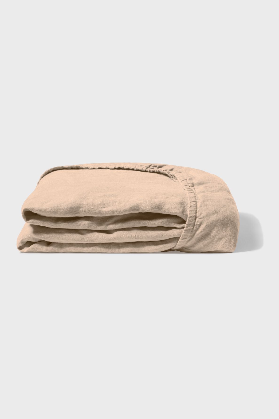 A neatly folded light beige fitted bed sheet, displayed against a plain white background with a subtle shadow on the right side.
