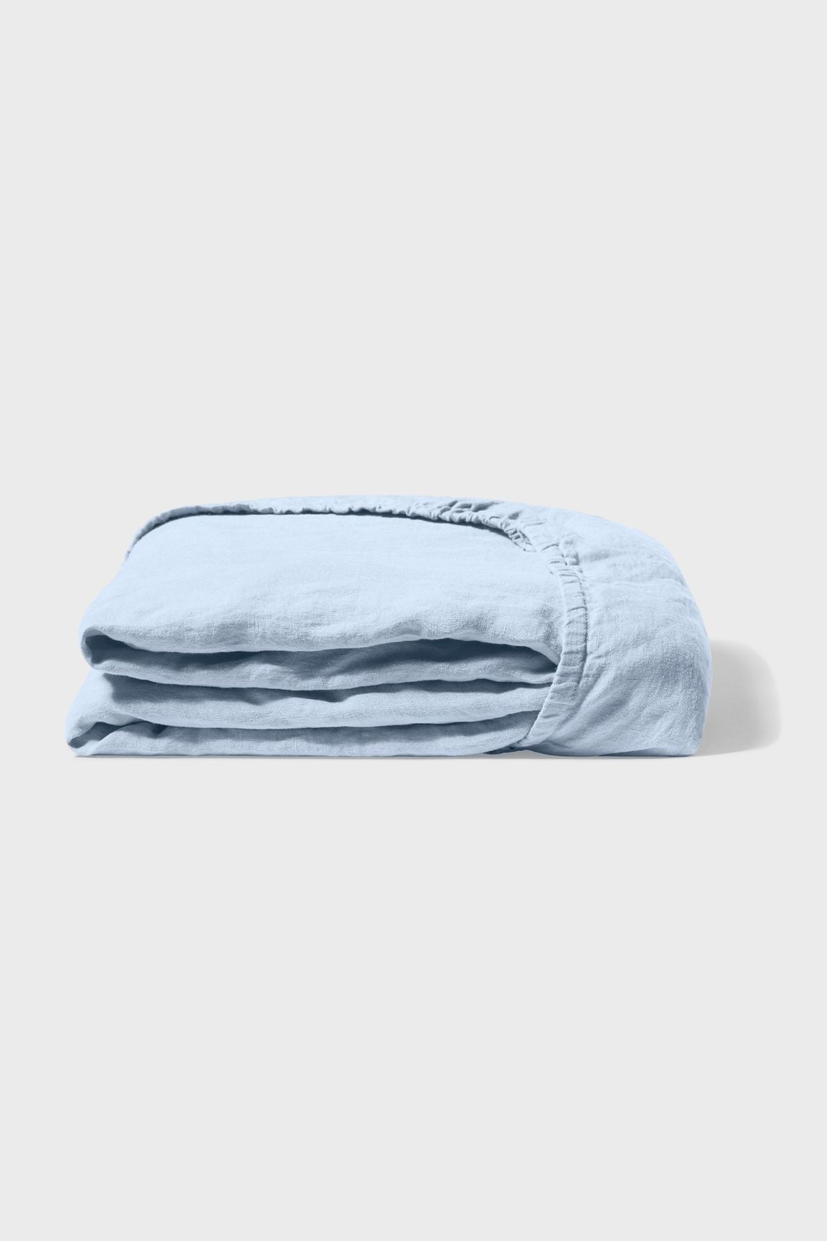 A neatly folded light blue fitted sheet made of soft fabric is placed on a plain white surface, with the elastic edge visible.