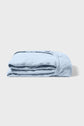 A neatly folded light blue fitted sheet made of soft fabric is placed on a plain white surface, with the elastic edge visible.