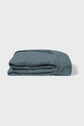 A folded blue fitted bed sheet lies on a plain white background, showing its elastic edge and soft fabric texture.