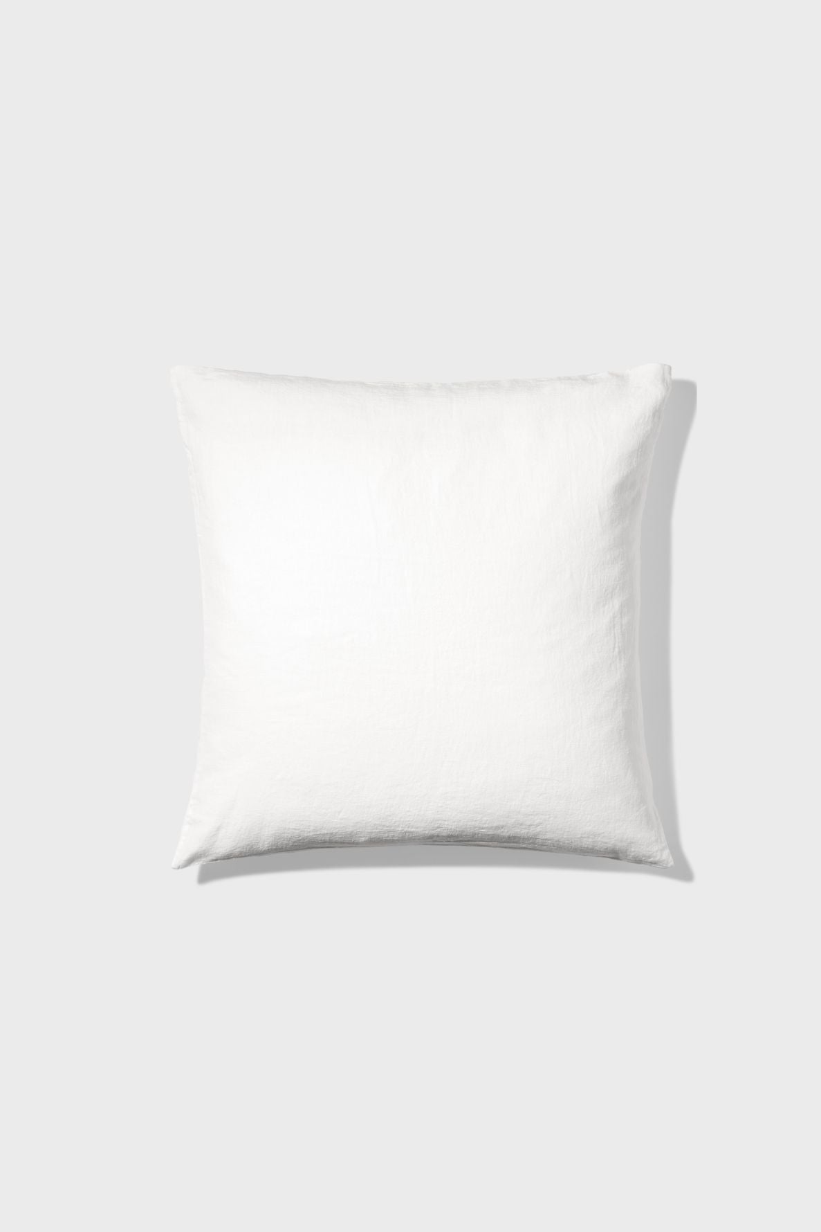 A plain white square pillow is centered on a light gray background, casting a soft shadow to the right.