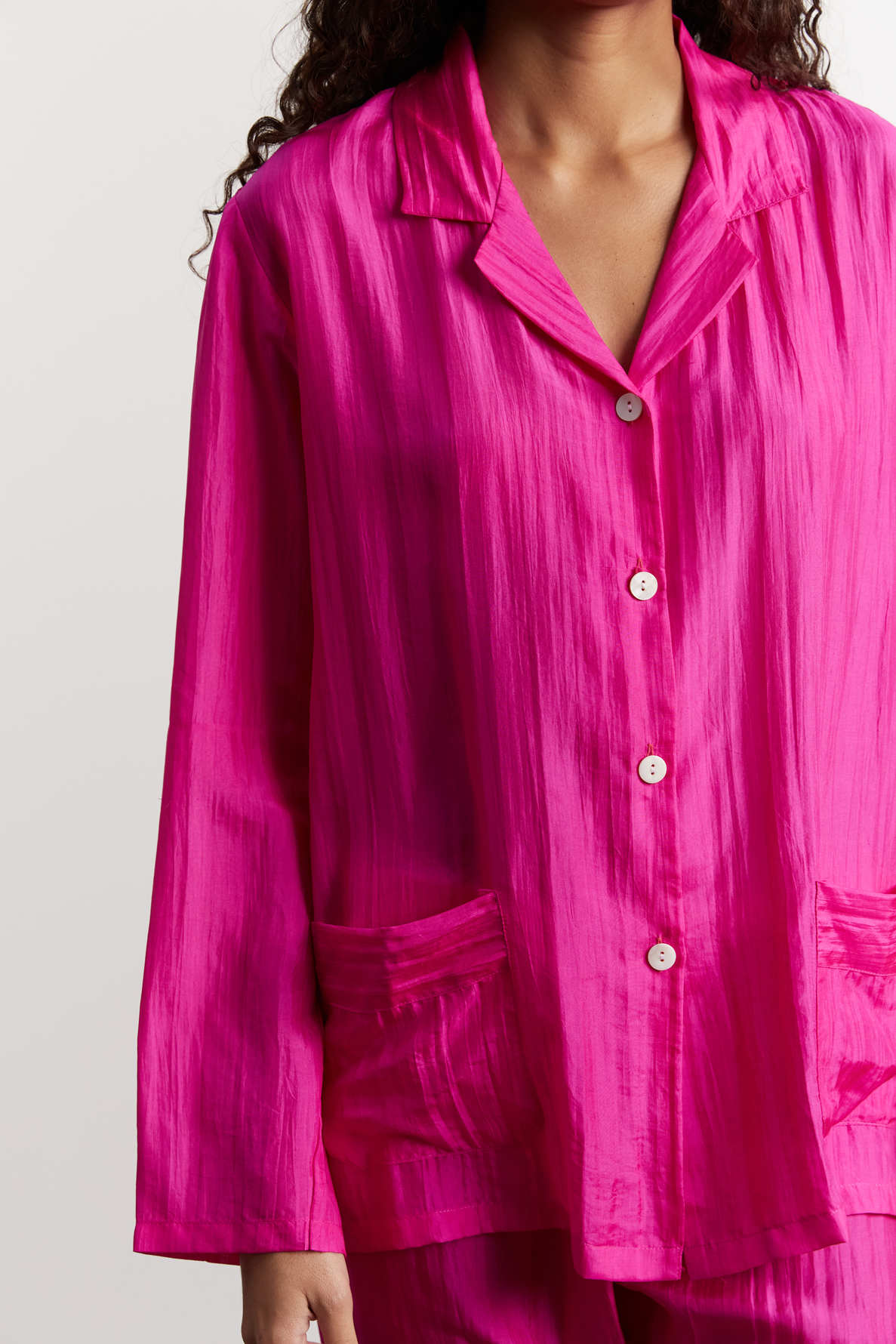 A person wearing a bright pink, long-sleeve, button-up pajama top with two front pockets, shown from shoulders to thighs against a plain background.