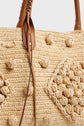 Close-up of a woven sac à main raphia tote bag with textured, knotted patterns and leather handles featuring stitched detailing and a leather tie accent.