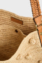 Close-up of an open woven straw bag with tan braided leather handles in cuir tressé artisanal and a brown leather label inside reading GERARD DAREL. The bag features textured woven patterns, decorative elements, and the charming appeal of a totebag raphia naturel.