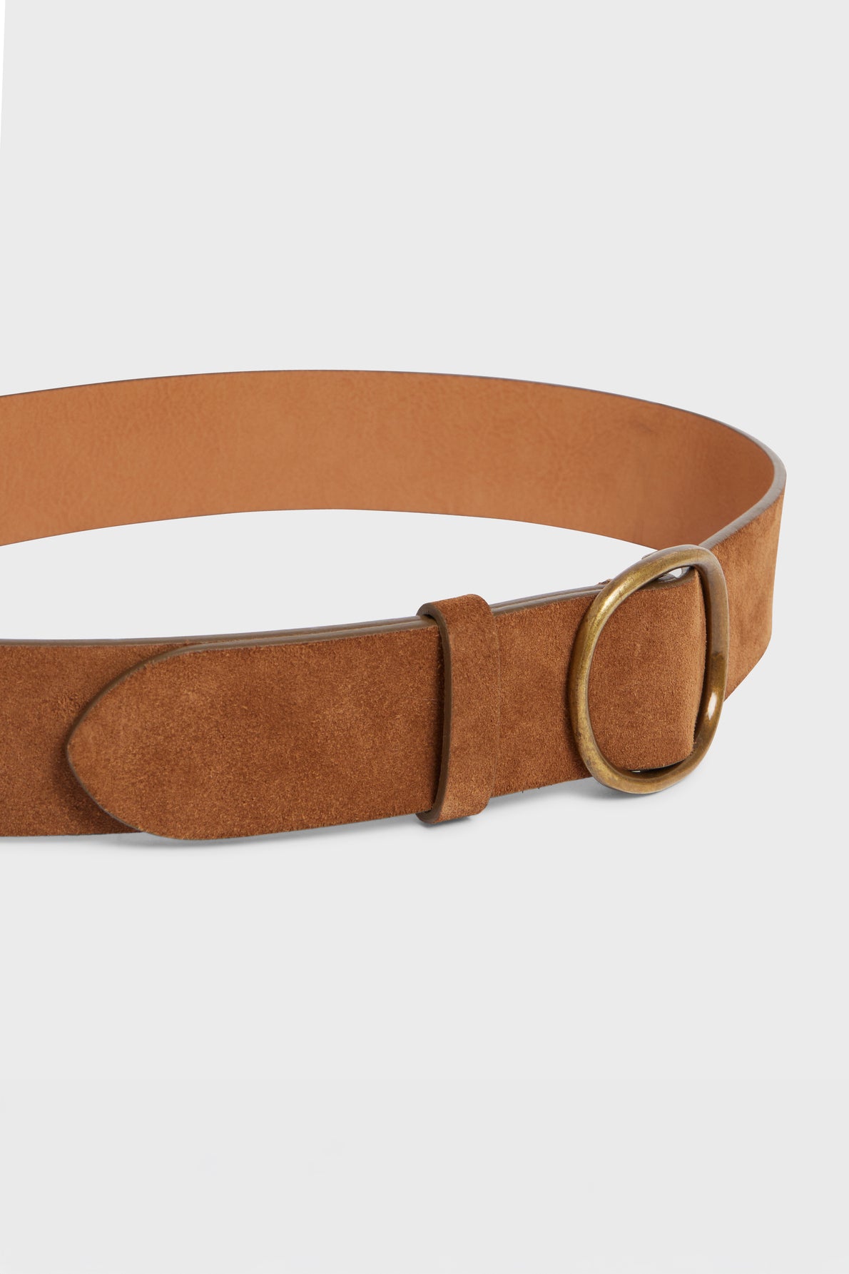 A brown cuir velours belt with a gold oval boucle coulissante, shown on a plain light gray background for a ceinture minimaliste look.