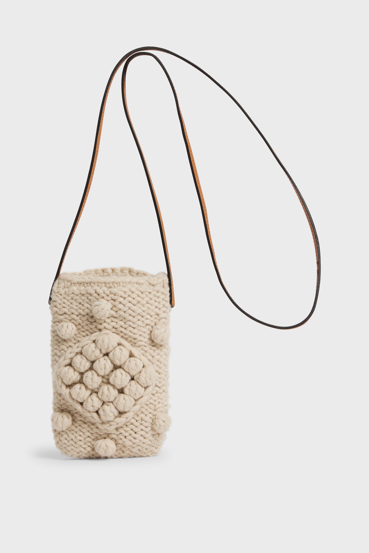 A small beige tricot de laine crossbody bag with a motif losange and raised bobbles, featuring a long brown leather strap—perfect as a chic porte téléphone.