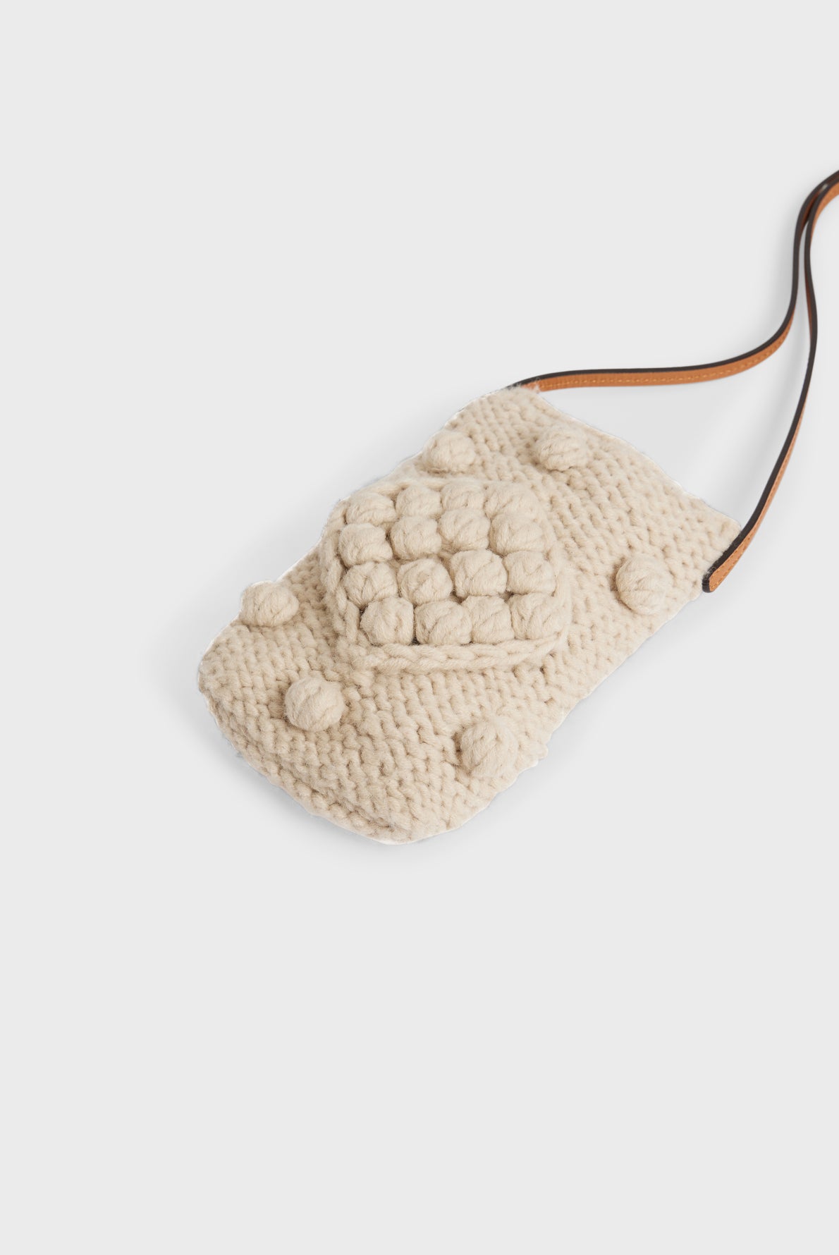 A small, cream-colored, knitted pouch crafted from soft tricot de laine, featuring raised circular patterns and a brown strap, displayed on a plain white background.