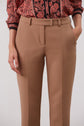 A person wears tan dress pants with hands in the pockets and a patterned red and black long-sleeve shirt tucked in. The upper body is partially visible against a plain background.