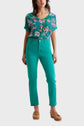 A woman stands facing forward, wearing a teal floral top, teal high-waisted pants, and tan clogs, against a plain light background.