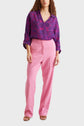 A person wearing a purple floral blouse with rolled sleeves and a pantalon tailleur rose taille haute, standing against a plain light background.