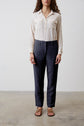 A person stands against a plain background wearing a cream long-sleeve blouse, dark trousers, and brown sandals. The image is cropped at the neck, so their full face is not visible.