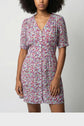 Woman wearing a short-sleeved, buttoned robe mi-longue with a colorful motif floral pattern, standing against a plain light background. Her face is partially out of the frame.