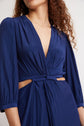 A person with long, wavy hair wears a deep blue, v-neck dress with three-quarter sleeves and side cutouts. The focus is on the dresss texture and design, as the face is partially out of frame.