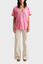 Woman wearing a loose pink V-neck T-shirt, off-white wide-leg pants, and brown platform shoes, standing against a plain light background.