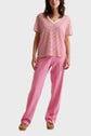 Woman wearing a red and white striped V-neck short sleeve top, loose pink pants, and brown sandals, standing against a plain light background.