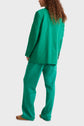 Person with long curly hair wears a loose-fitting green suit and brown shoes, standing with their back to the camera against a plain white background.